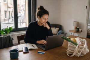 Remote worker using a laptop at a dining table with groceries in a temporary apartment